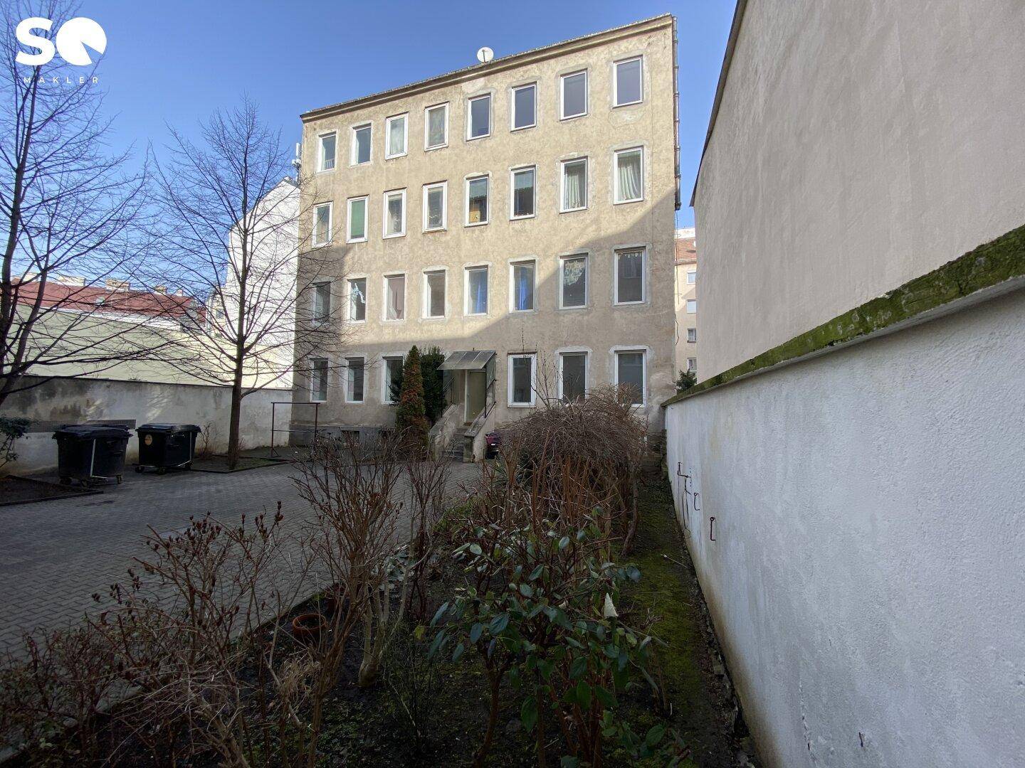 Gebäudefassade eines Mehrfamilienhauses von einem Hinterhof aus gesehen mit kahlen Bäumen.