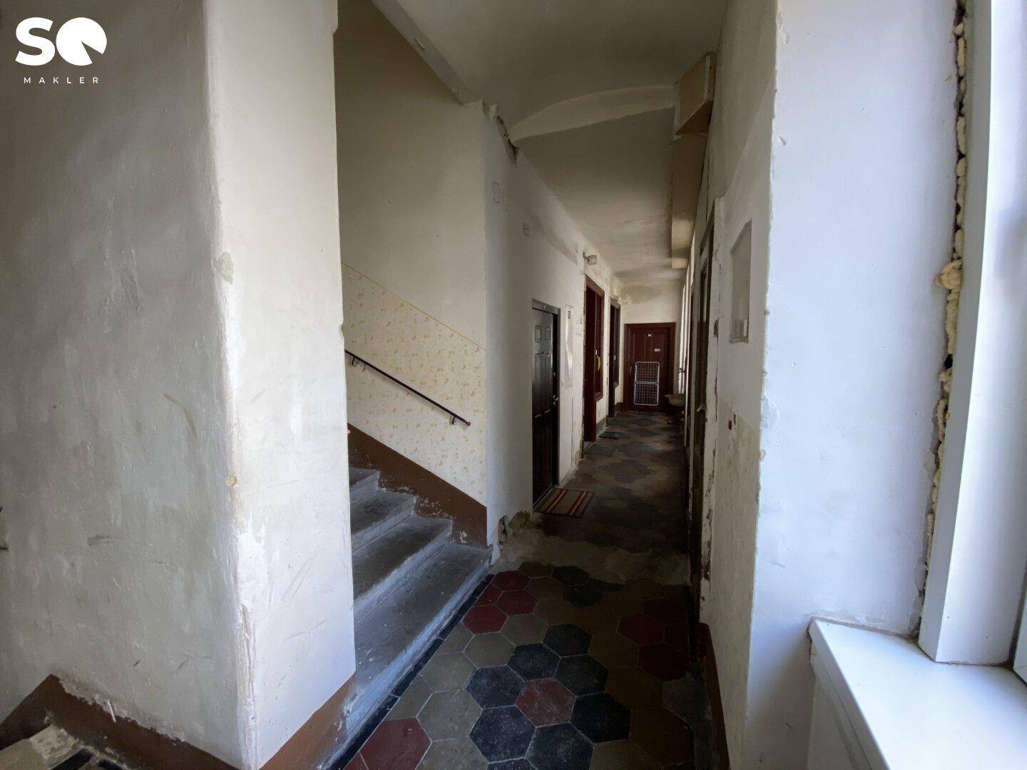 Gemeinschaftlicher Flur mit Treppenaufgang, alten Fliesen und mehreren Wohnungstüren.