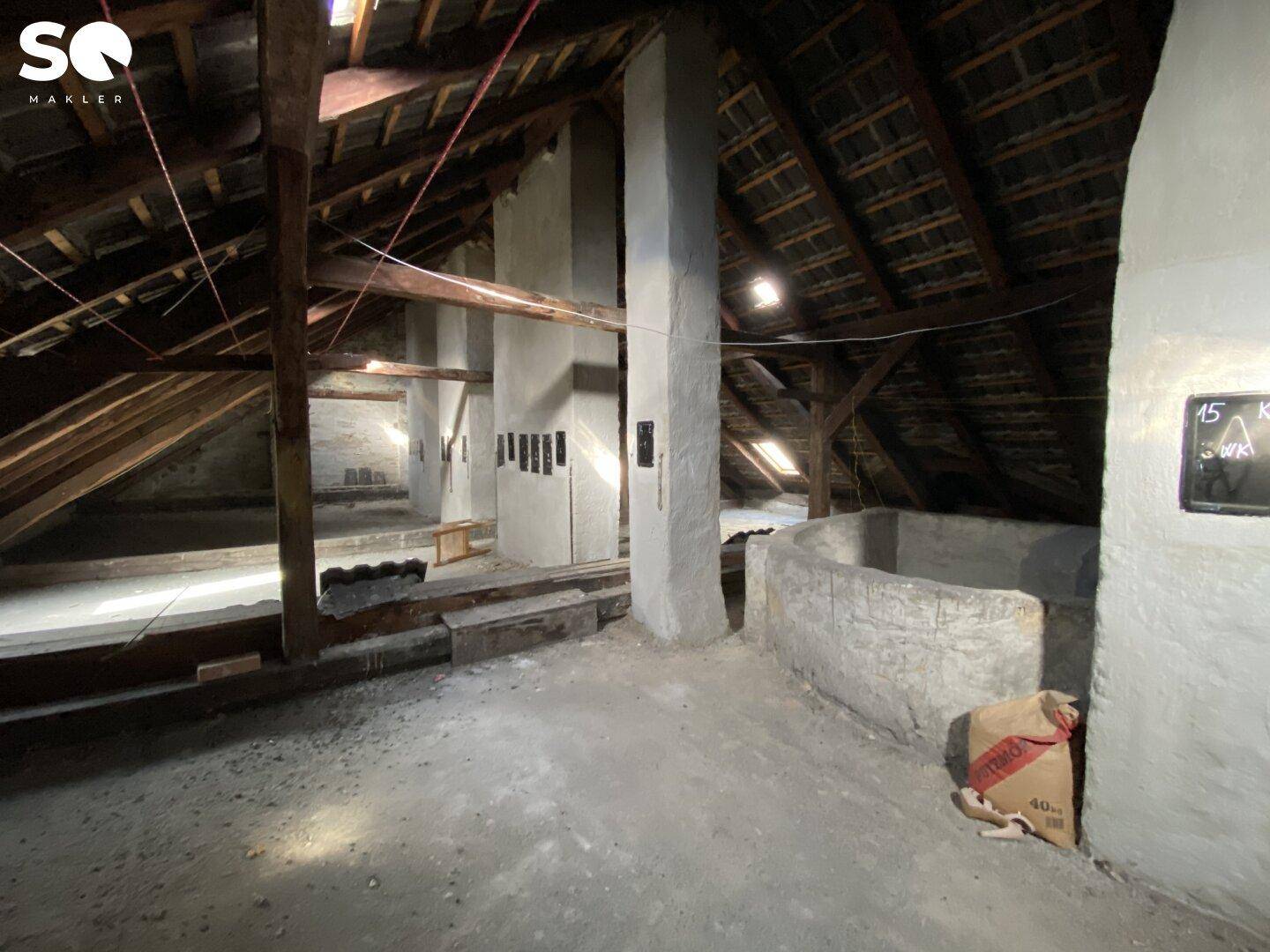 Unausgebauter Dachboden mit sichtbaren Holzbalken und Betonboden, bietet Ausbaupotenzial.
