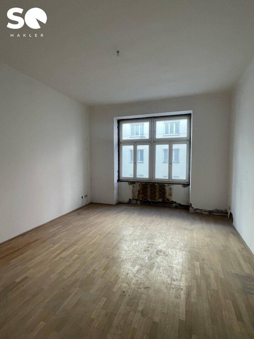 Helles Zimmer mit Fischgrätparkettboden und einem großen Fenster, das viel Licht hereinlässt.