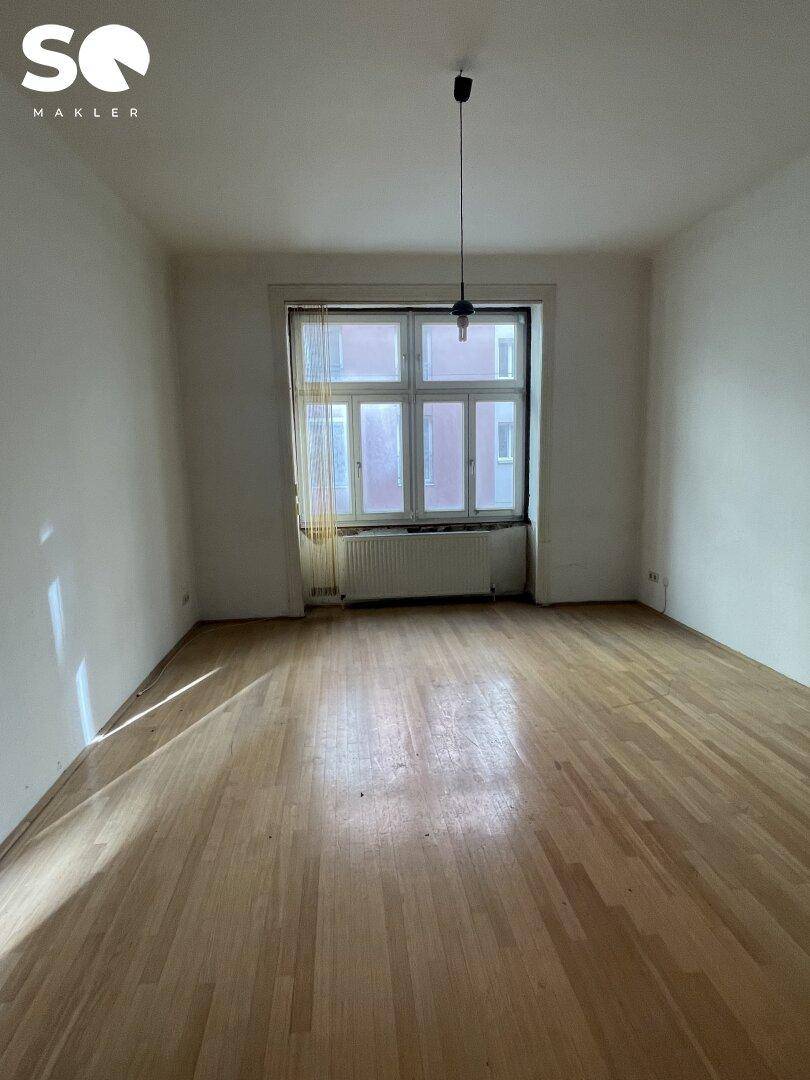 Lichtdurchflutetes Zimmer mit klassischem Parkettboden und einem Fenster mit Heizkörper.
