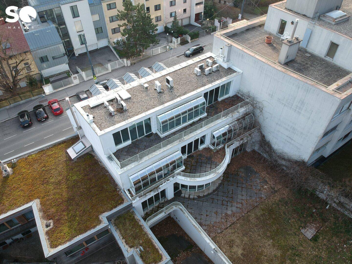 Luftaufnahme eines Gebäudes mit Flachdach, Terrassen und großen Fensterfronten in urbaner Umgebung.