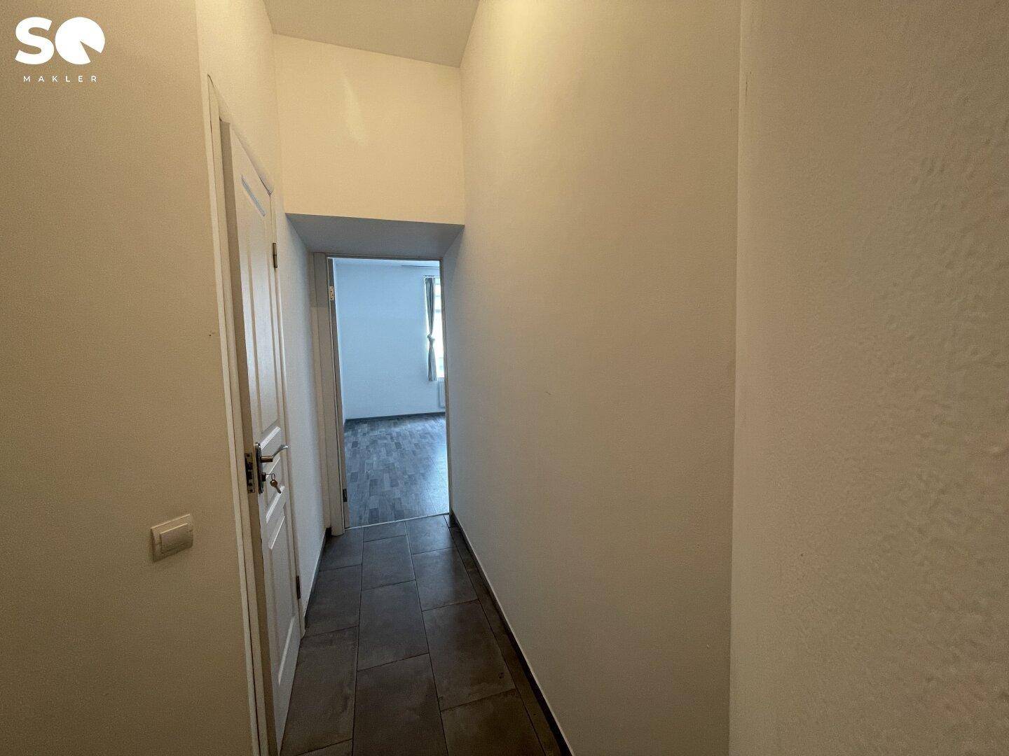 Schmaler Flur mit Fliesenboden und weiß gestrichenen Wänden, der zu weiteren Räumen führt.