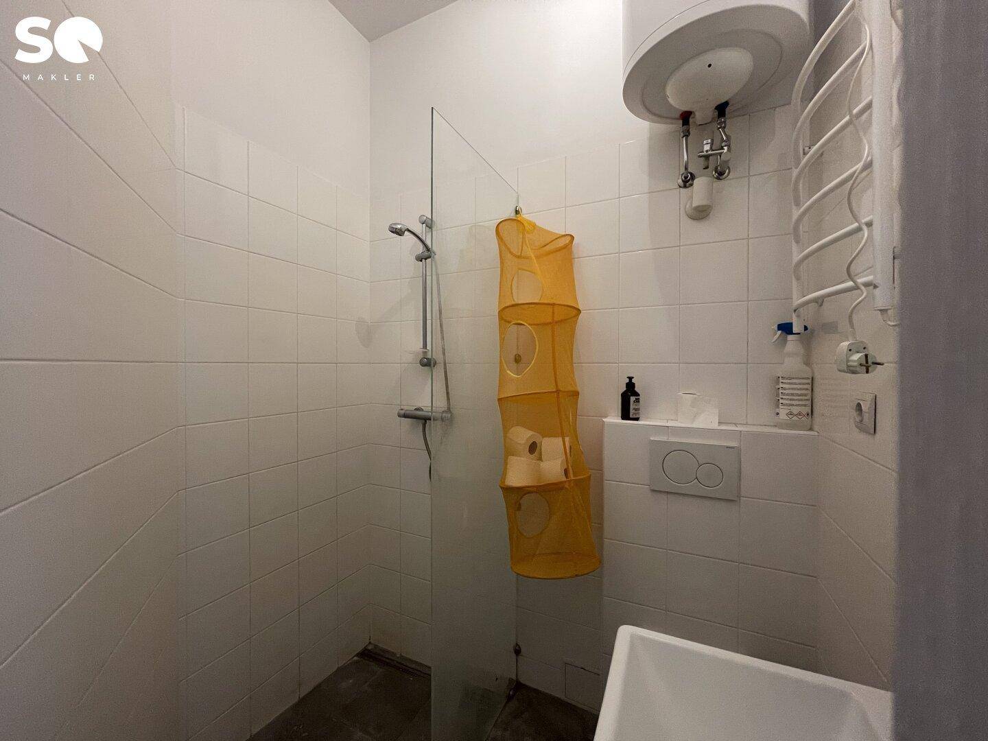 Duschbereich im Badezimmer mit weißen Fliesen, Glasabtrennung und einem Warmwasserboiler.