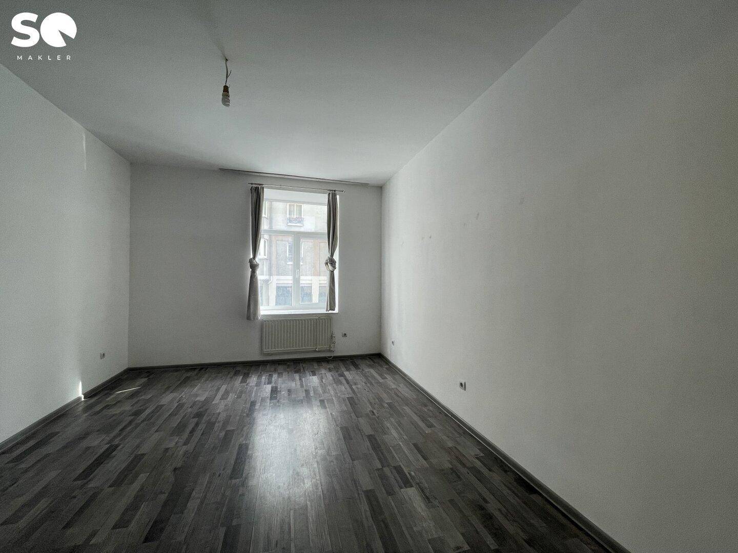 Heller, unmöblierter Raum mit Laminatboden, einem Fenster und einem Heizkörper.