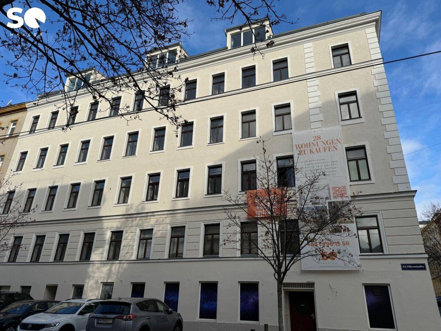 Nahaufnahme der frisch renovierten Fassade eines Mehrfamilienhauses mit Verkaufsbannern.