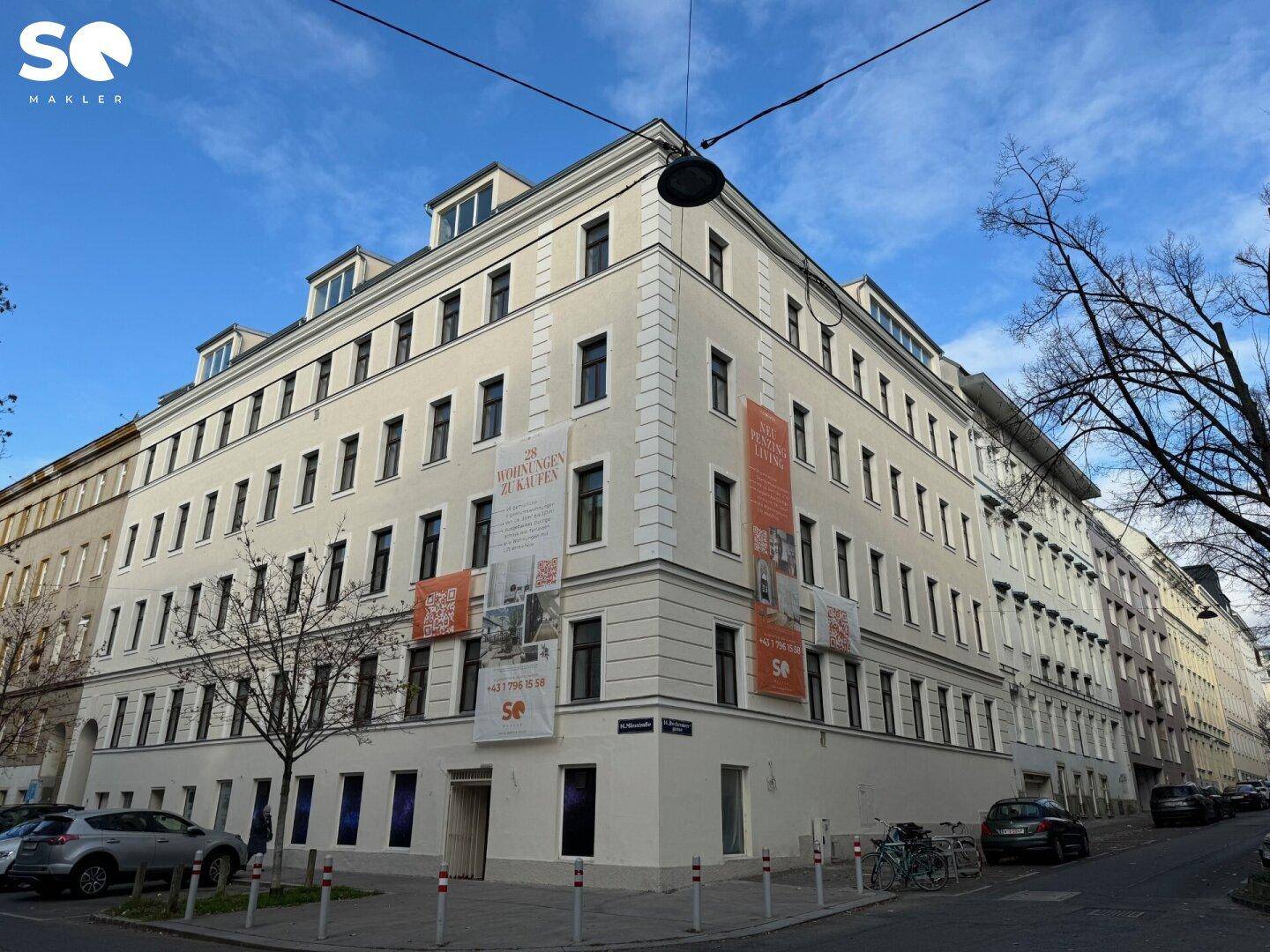 Großes Eckgebäude mit vielen Fenstern und Werbebannern an einer städtischen Straße.