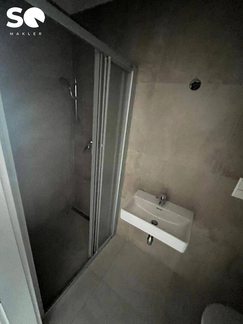 Modernes Badezimmer mit Duschkabine, Wandwaschbecken und grauen Fliesen.