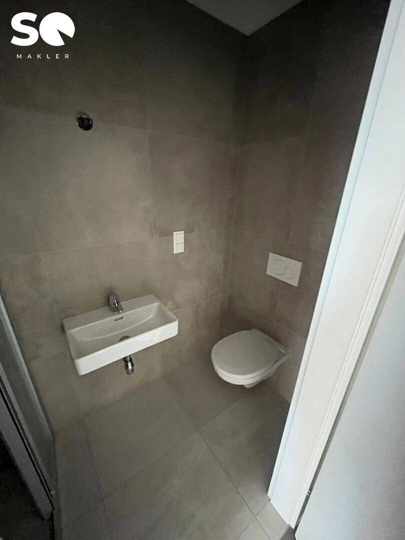 Kleines Gäste-WC mit Wand-WC, Waschbecken und modernen grauen Fliesen.