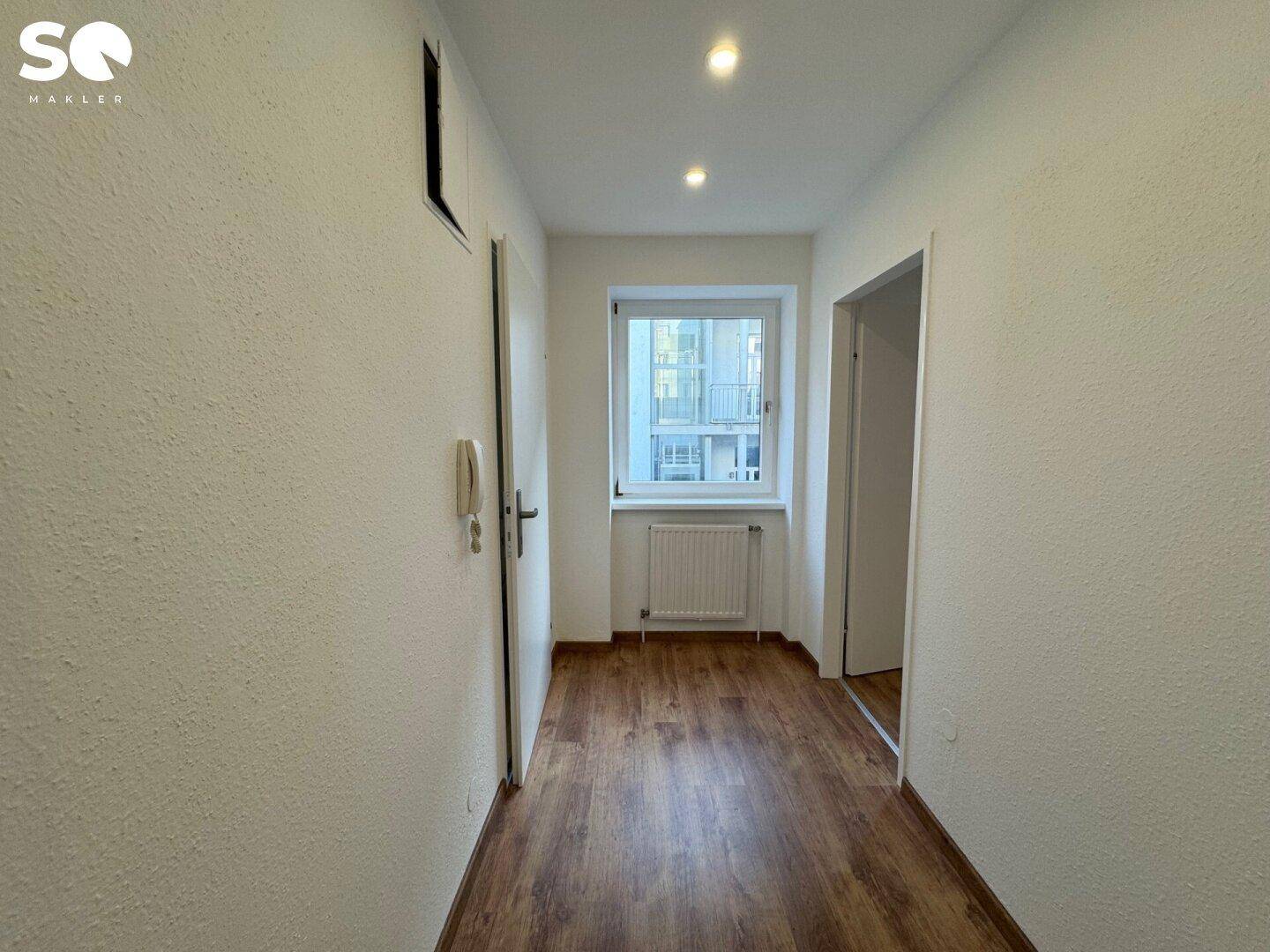 Heller Flur mit Laminatboden, Gegensprechanlage und Fenster, verbindet die Wohnbereiche.