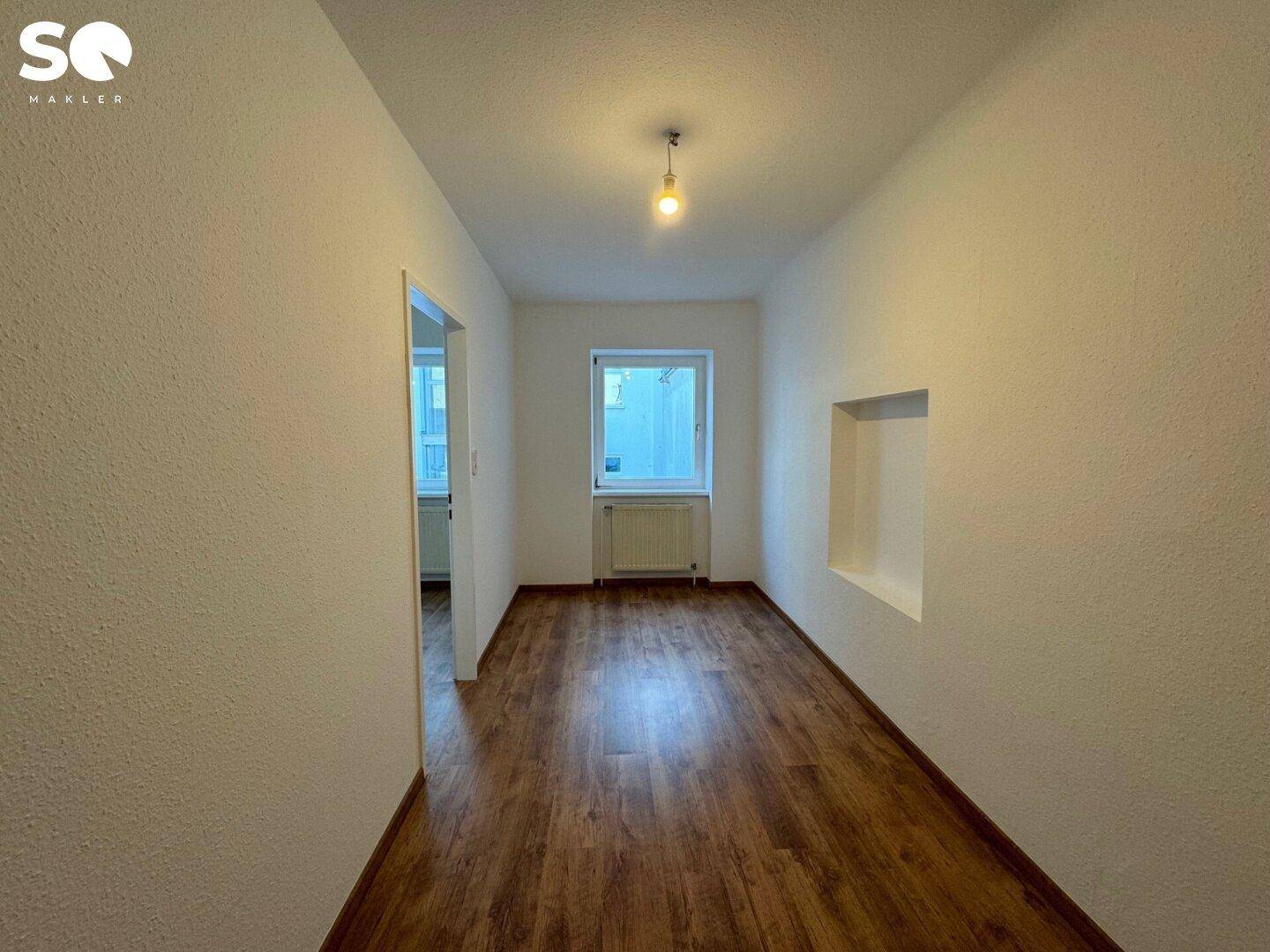 Langer, heller Raum mit Laminatboden und einem Fenster, bietet vielseitige Nutzungsmöglichkeiten.