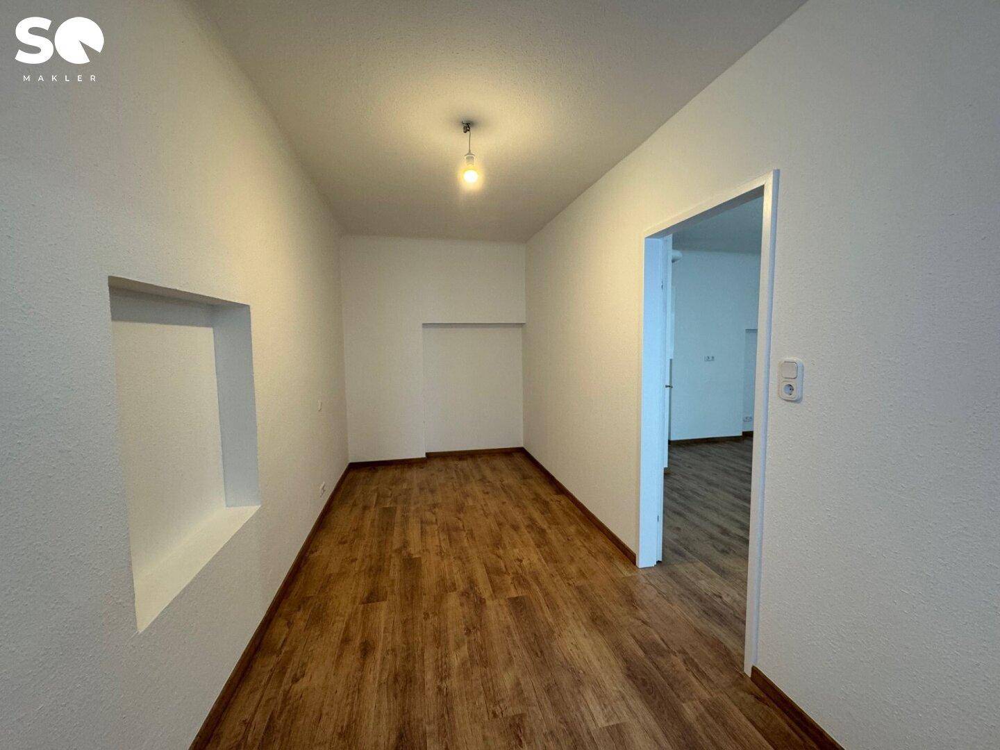 Schmaler Raum mit Laminatboden und einer Wandnische, ideal für Stauraum oder Dekoration.