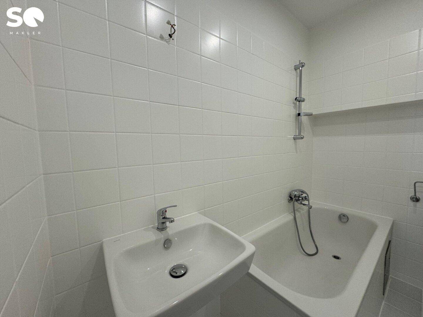 Modern gefliestes Badezimmer mit Badewanne, Duschvorrichtung und Waschbecken in Weiß.