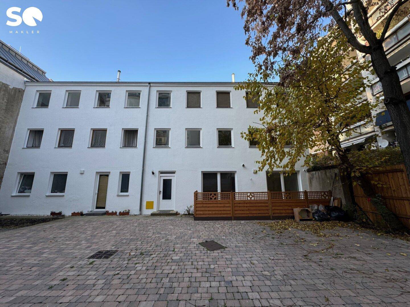 Hinterhof mit gepflasterter Fläche und einer kleinen Terrasse im Erdgeschoss.