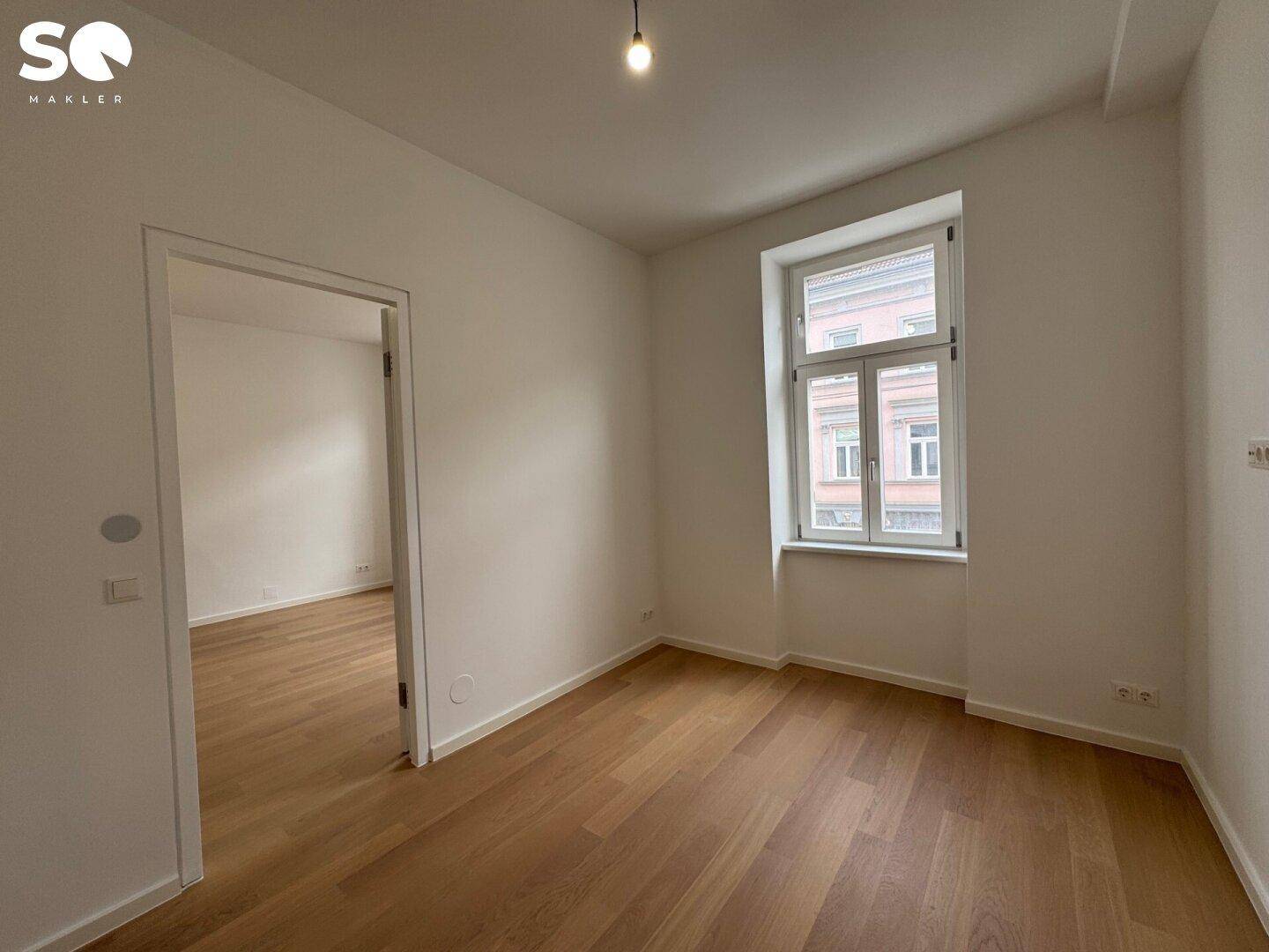 Gemütliches Zimmer mit Holzboden und einem großen Fenster, das viel Tageslicht bietet.