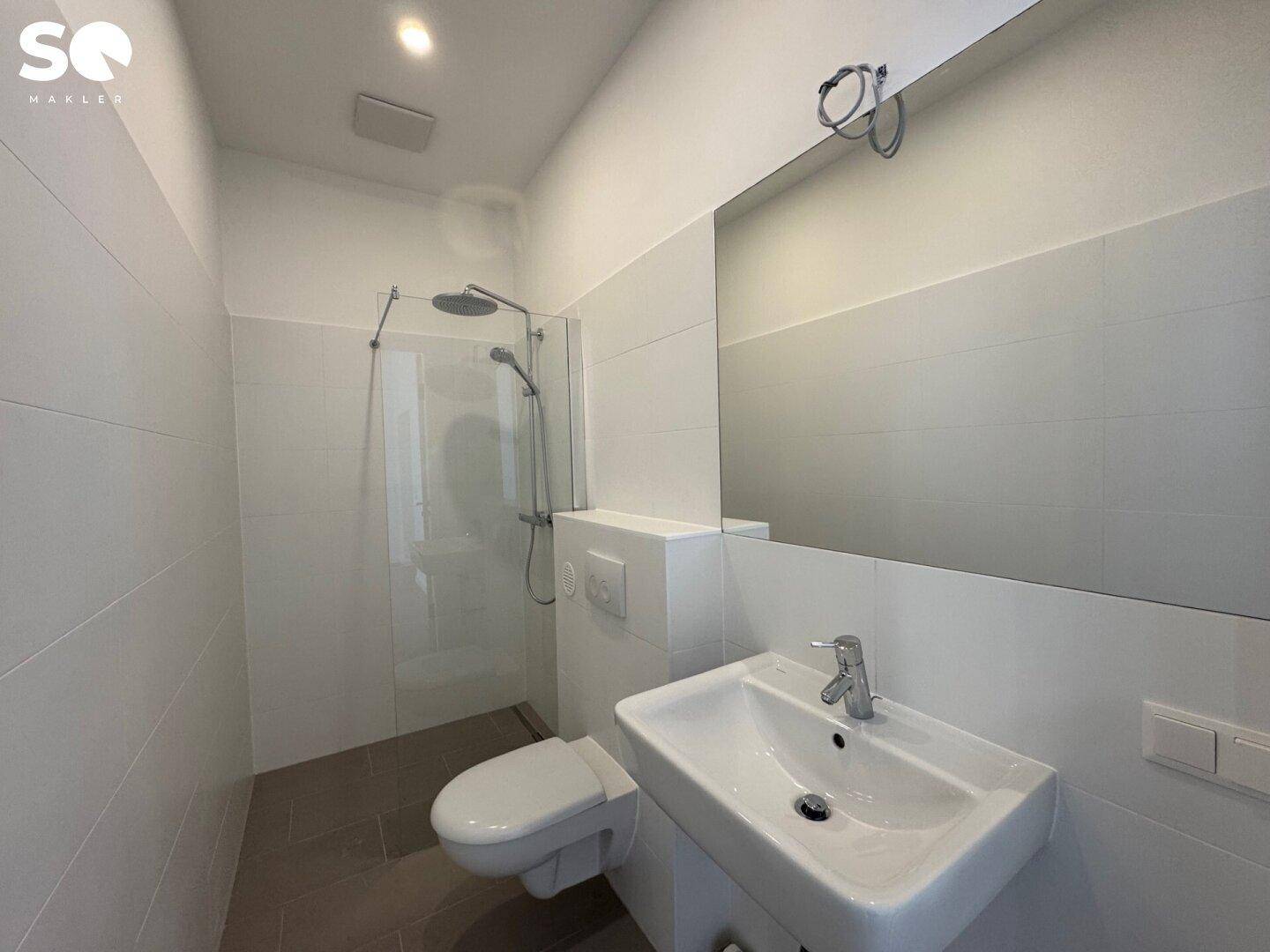 Modernes Badezimmer mit Dusche, wandhängendem WC und großem Spiegel über dem Waschbecken.