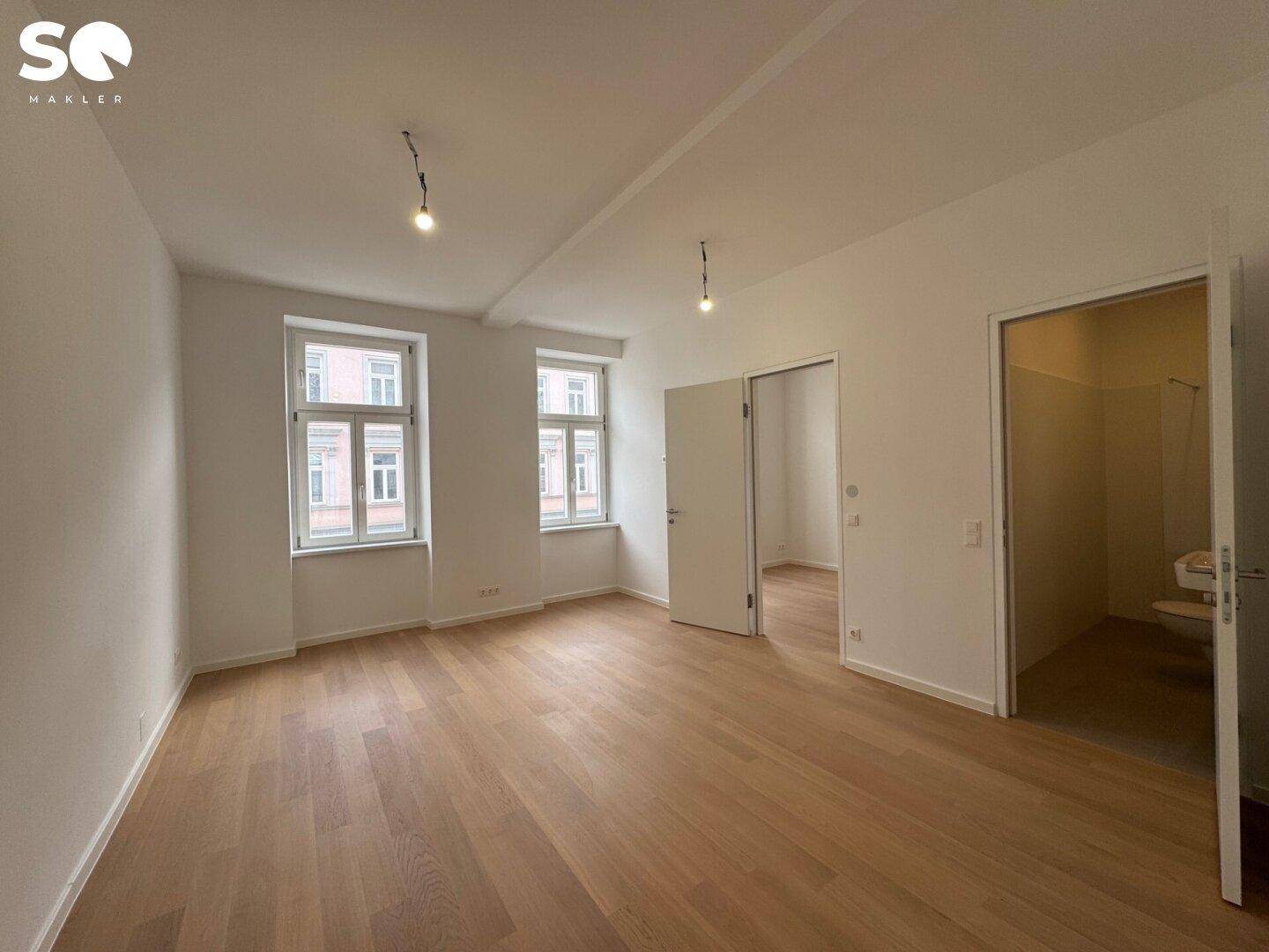 Geräumiges, helles Zimmer mit Holzboden und zwei Fenstern, die viel Tageslicht hereinlassen.