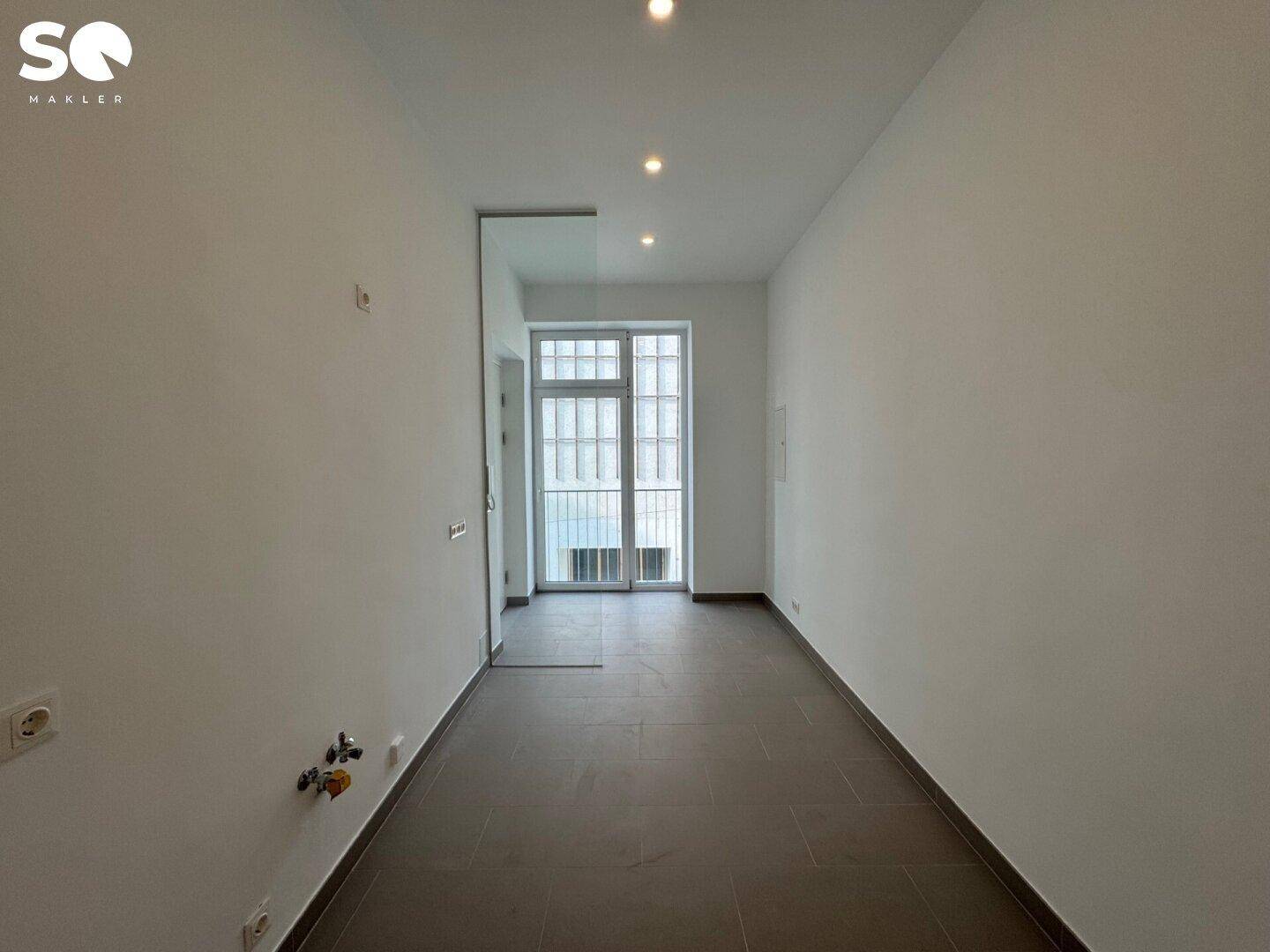 Langer, heller Flur mit Fliesenboden und einer Tür am Ende, die zu einem weiteren Raum führt.