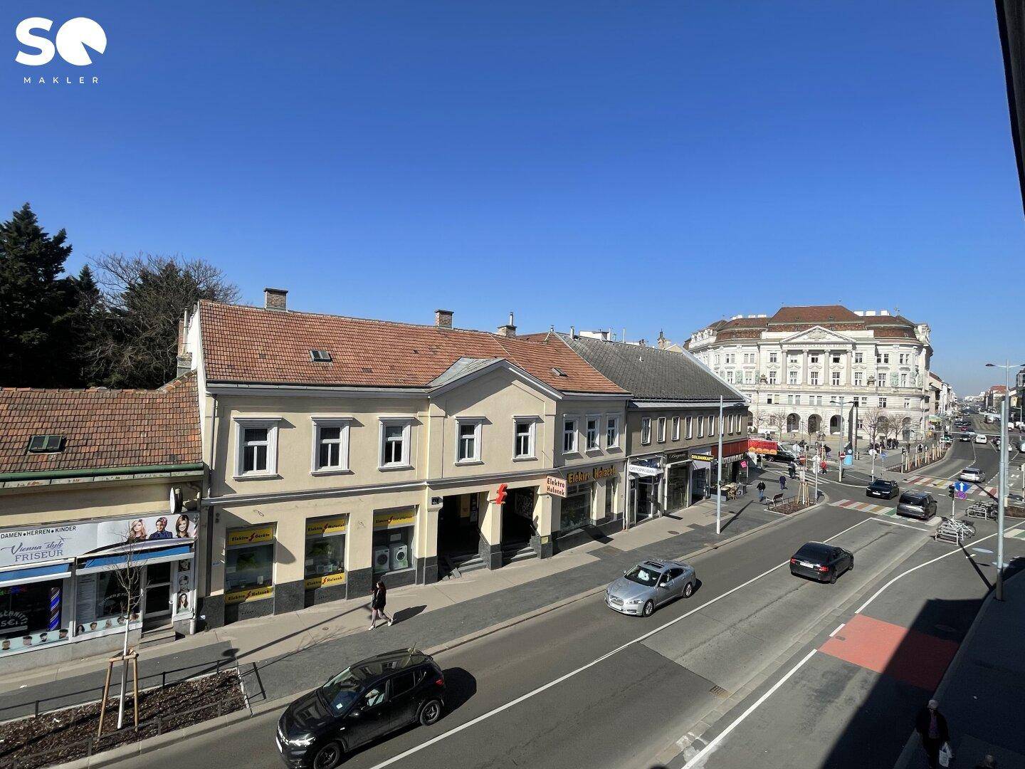 Weitläufiger Blick auf eine belebte Stadtstraße mit Geschäften und Gebäuden.