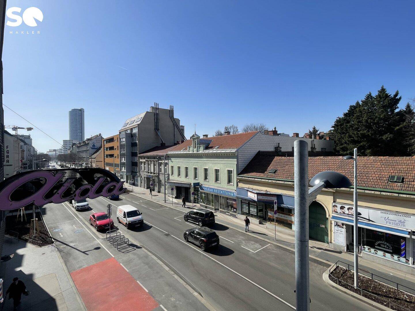 Panoramablick auf eine städtische Straße mit Geschäften und vorbeifahrenden Autos.