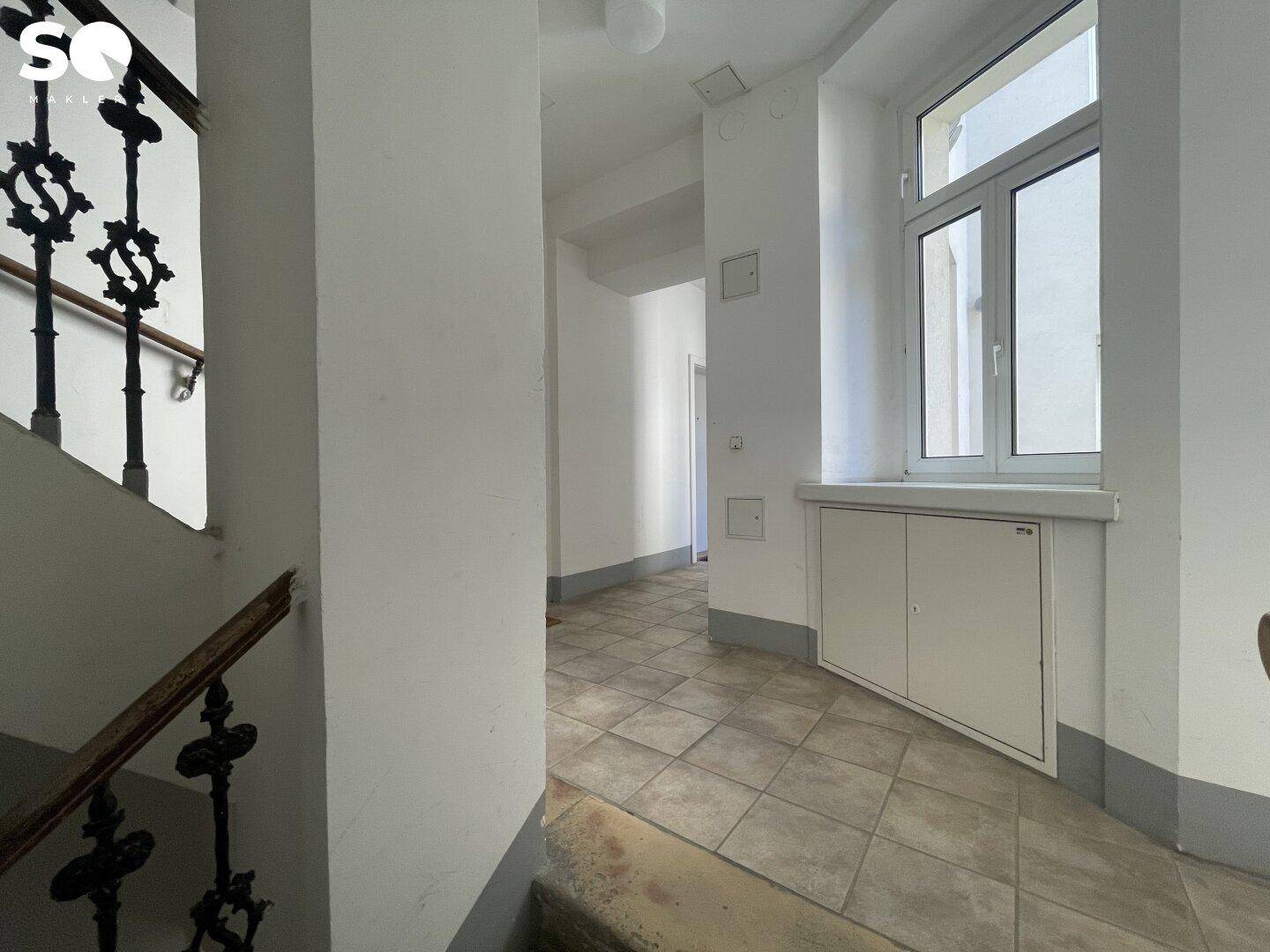 Helles Treppenhaus mit Fliesenboden, großem Fenster und einem klassischen schmiedeeisernen Geländer.