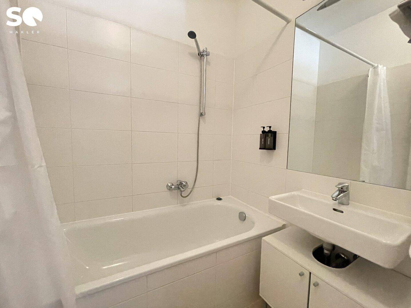 Funktionales Badezimmer mit Badewanne, integrierter Duschfunktion und hellen, weiß gefliesten Wänden.