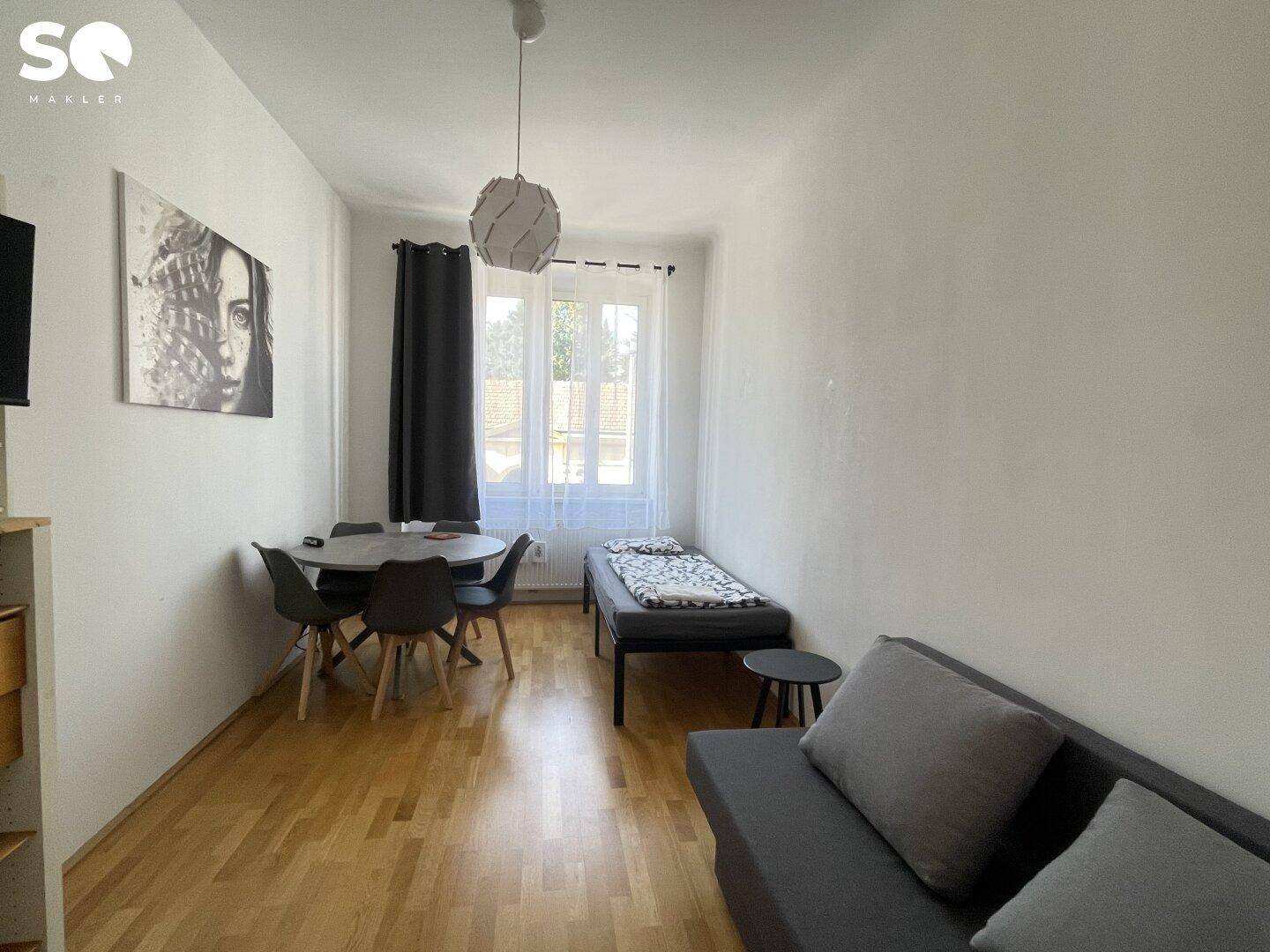 Heller Wohnbereich mit Sofa, Esstisch und Schlafgelegenheit, ideal für ein Studio-Apartment.