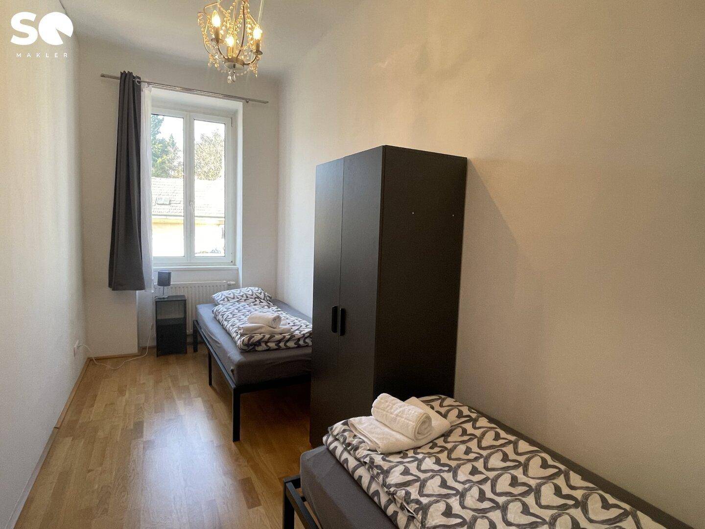 Schlafzimmer mit zwei Einzelbetten, Holzboden und einem Kronleuchter an der Decke.