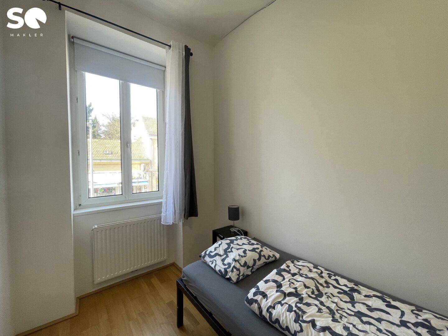 Helles Schlafzimmer mit Einzelbett, Holzboden und Fenster mit Blick ins Grüne.