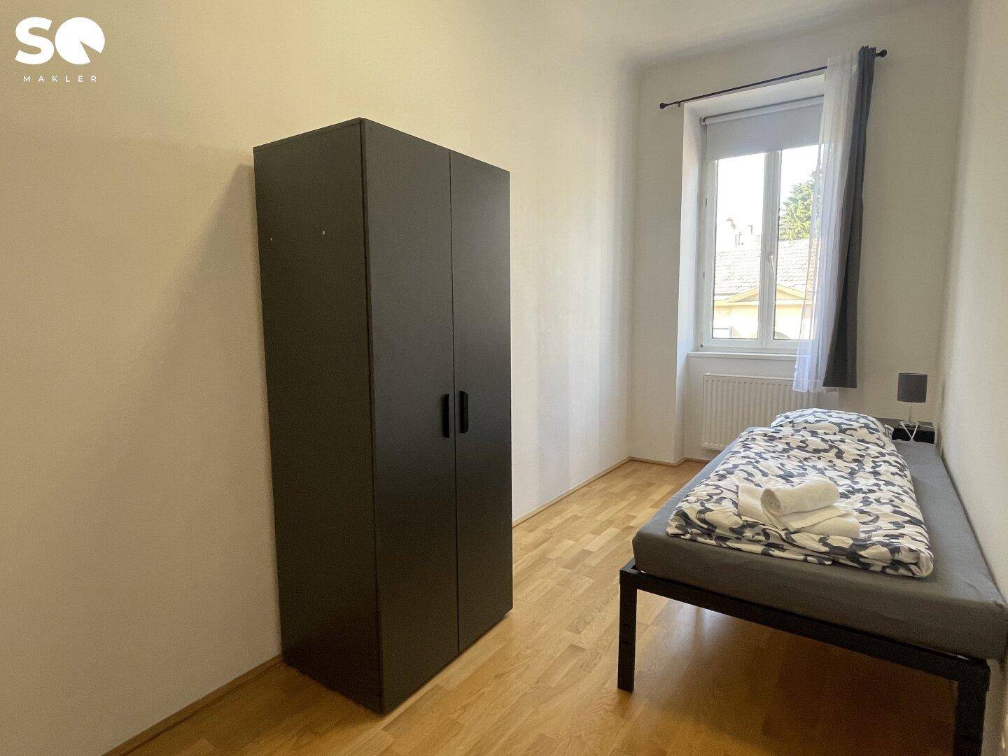 Gemütliches Schlafzimmer mit Einzelbett, dunklem Kleiderschrank und hellem Holzboden.