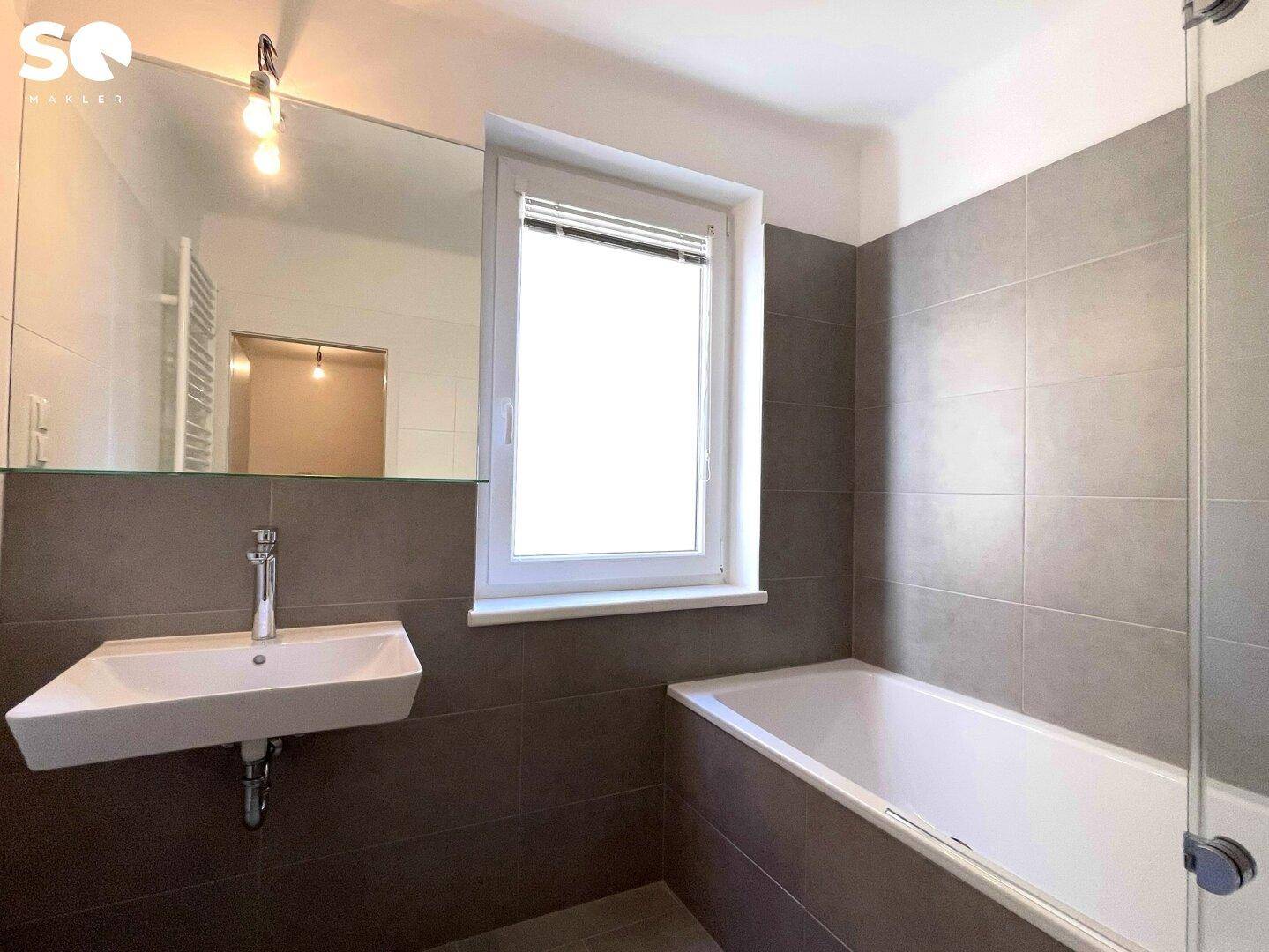 Helles Badezimmer mit Badewanne, modernem Waschbecken und Fenster für Tageslicht.