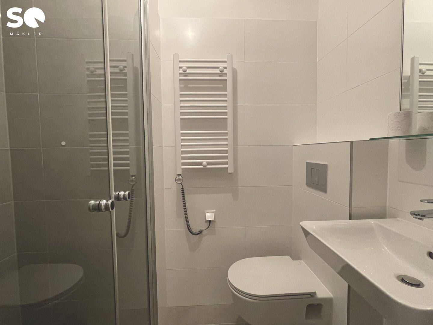Modernes WC mit Dusche, beheiztem Handtuchhalter und weißen Fliesen.