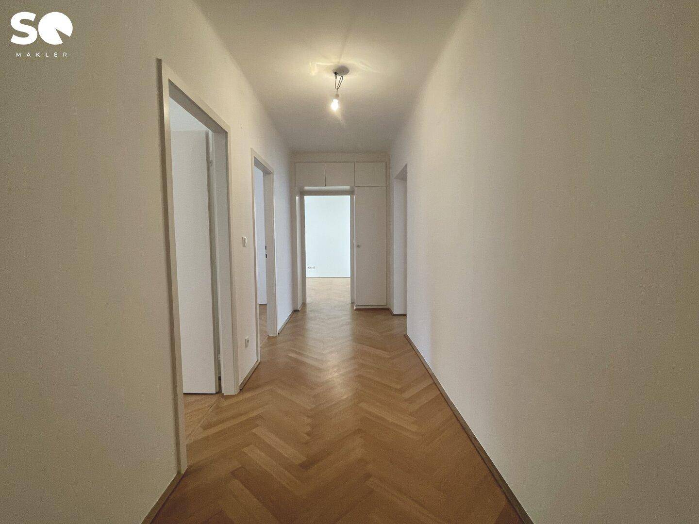 Heller Flur mit Fischgrätparkett, der zu verschiedenen Zimmern der Wohnung führt.