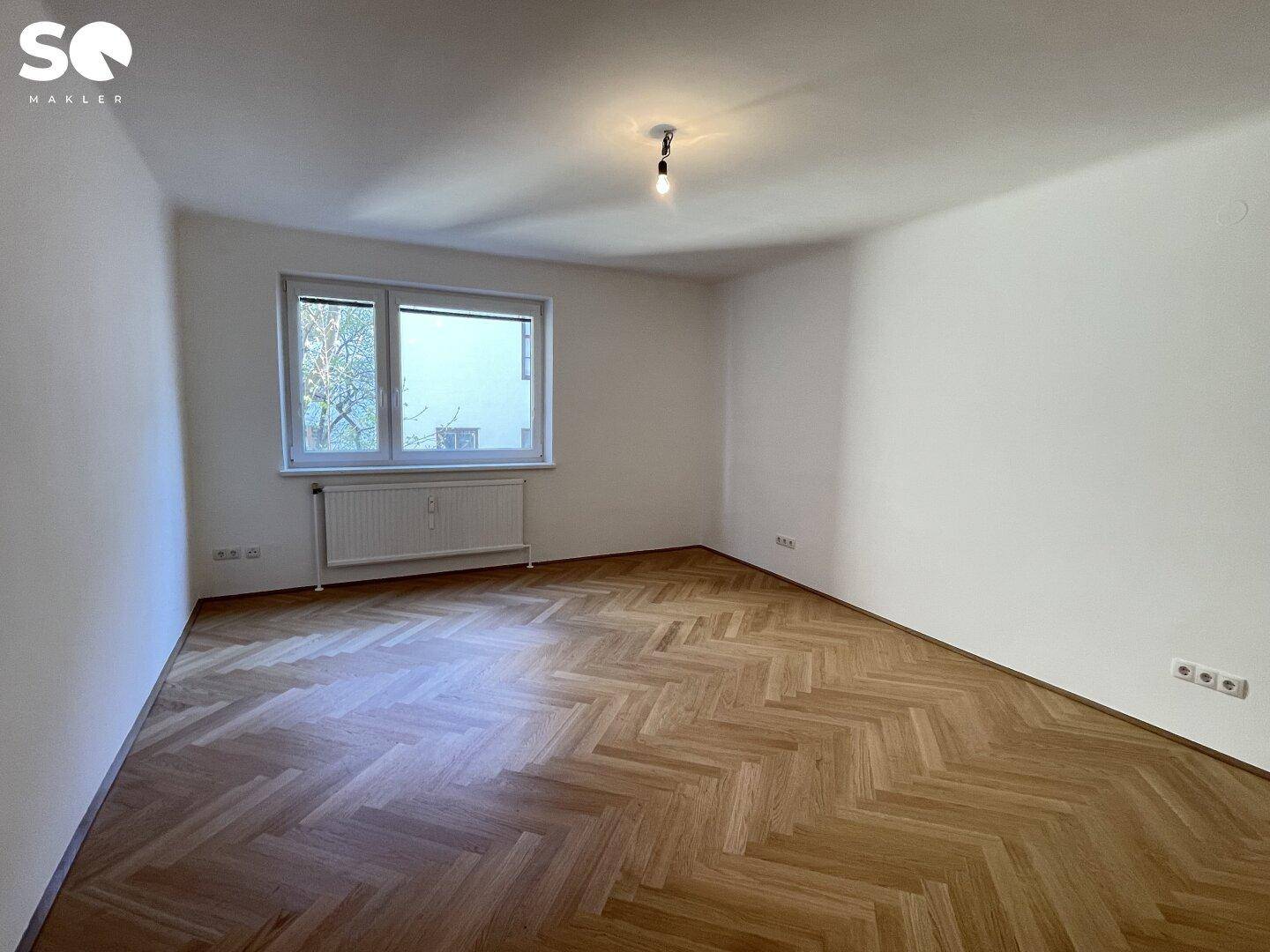Helles Zimmer mit Fischgrätparkett und großem Fenster, ideal als Schlaf- oder Arbeitszimmer.