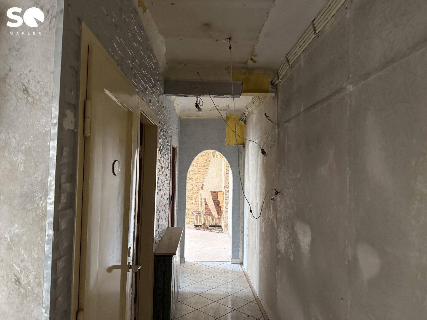 Langer Flur mit Fliesenboden, Steinwand und sichtbaren Elektroleitungen.