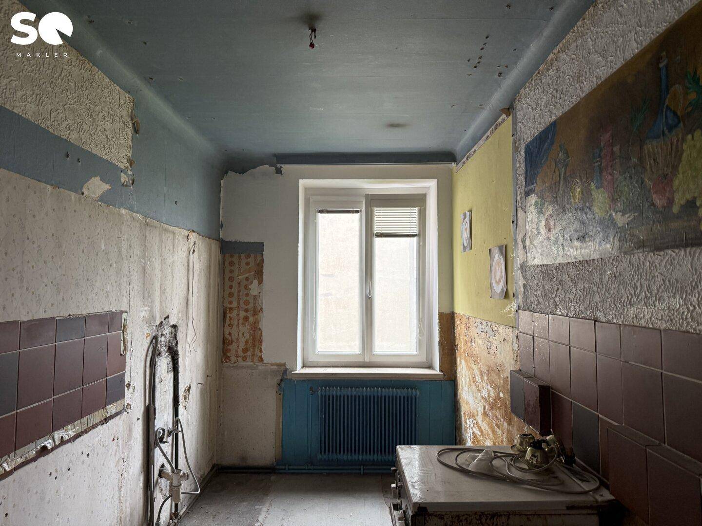 Alte Küche mit Fliesen, Heizkörper und Fenster, die eine vollständige Renovierung benötigt.