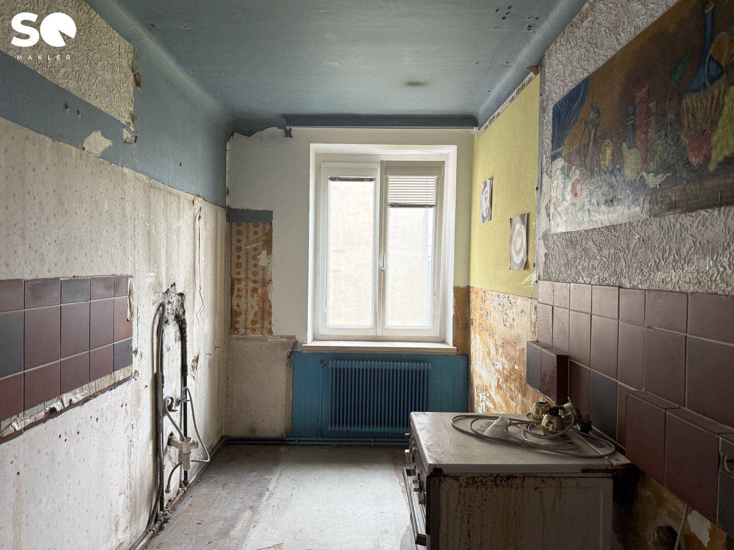 Renovierungsbedürftige Küche mit Fenster, Heizkörper und alten Wandfliesen.