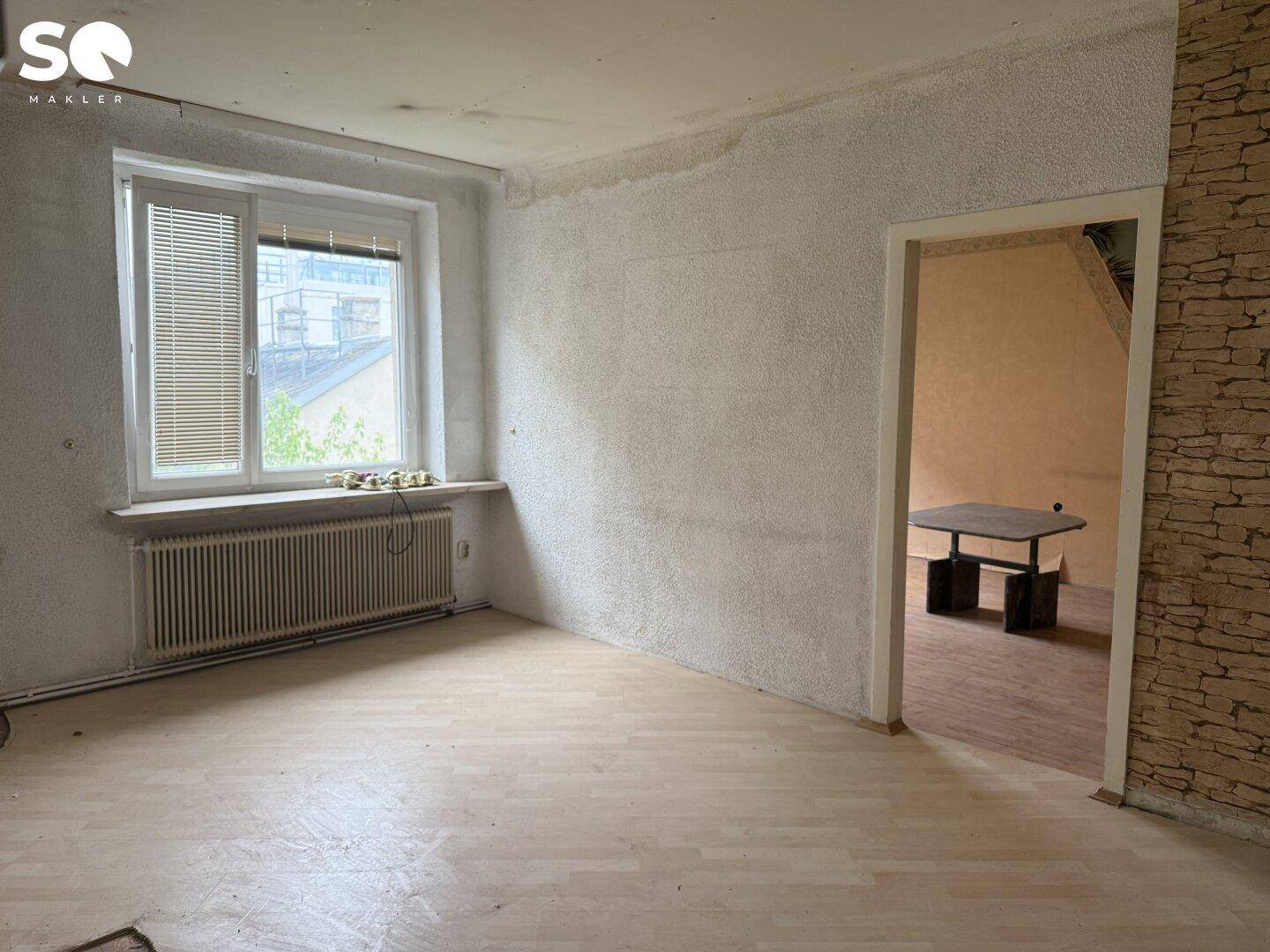 Heller Raum mit Fenster, Heizkörper und Holzboden, bereit für die Renovierung.