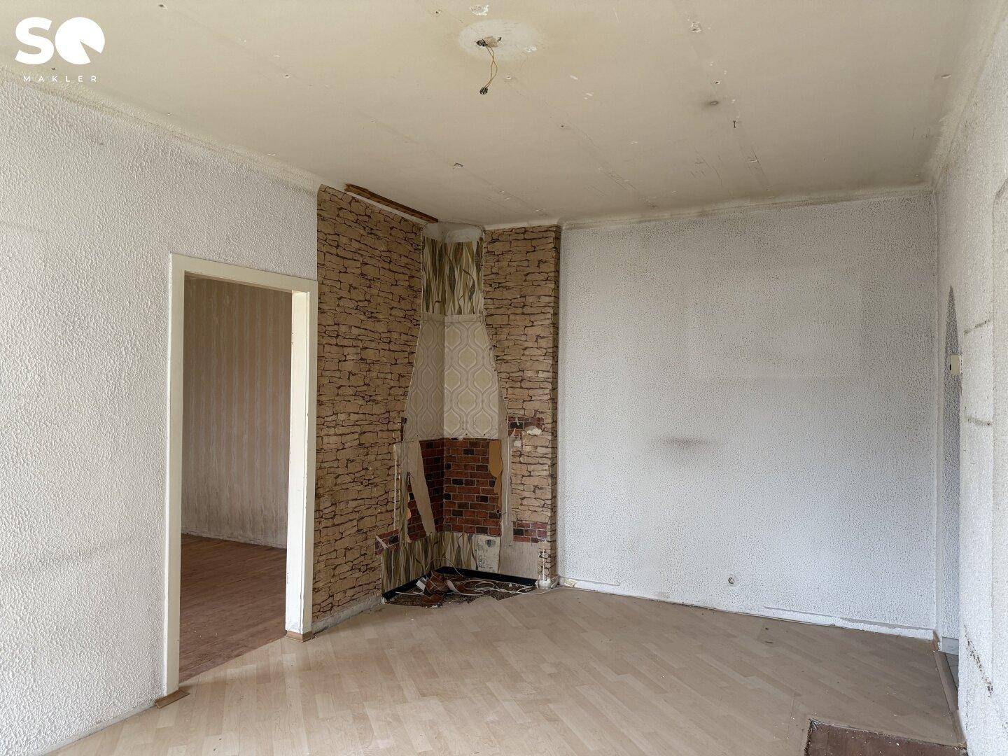 Wohnzimmer mit Kaminansatz, Holzboden und Wänden im Renovierungszustand.