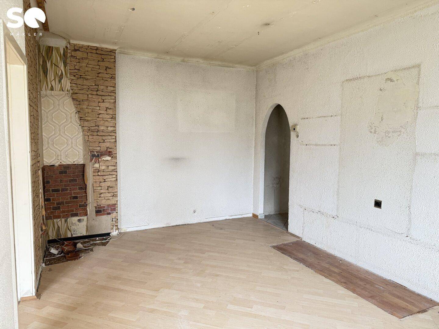 Renovierungsbedürftiger Raum mit Kaminansatz, Holzboden und einer Rundbogennische.