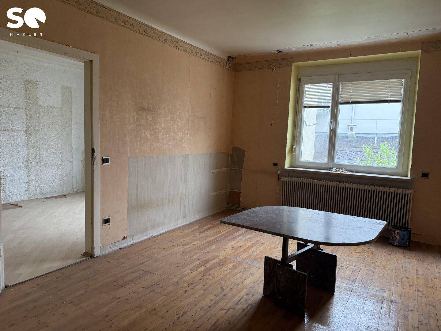 Esszimmer mit Holzboden, Fenster und Heizkörper, das eine Modernisierung benötigt.