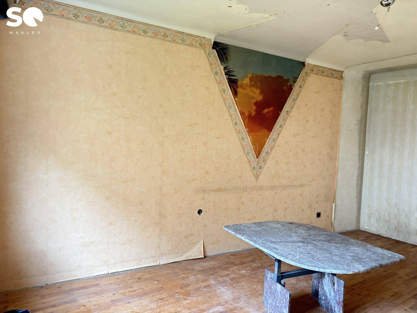Renovierungsbedürftiger Raum mit Holzboden und einer auffälligen Wanddekoration.