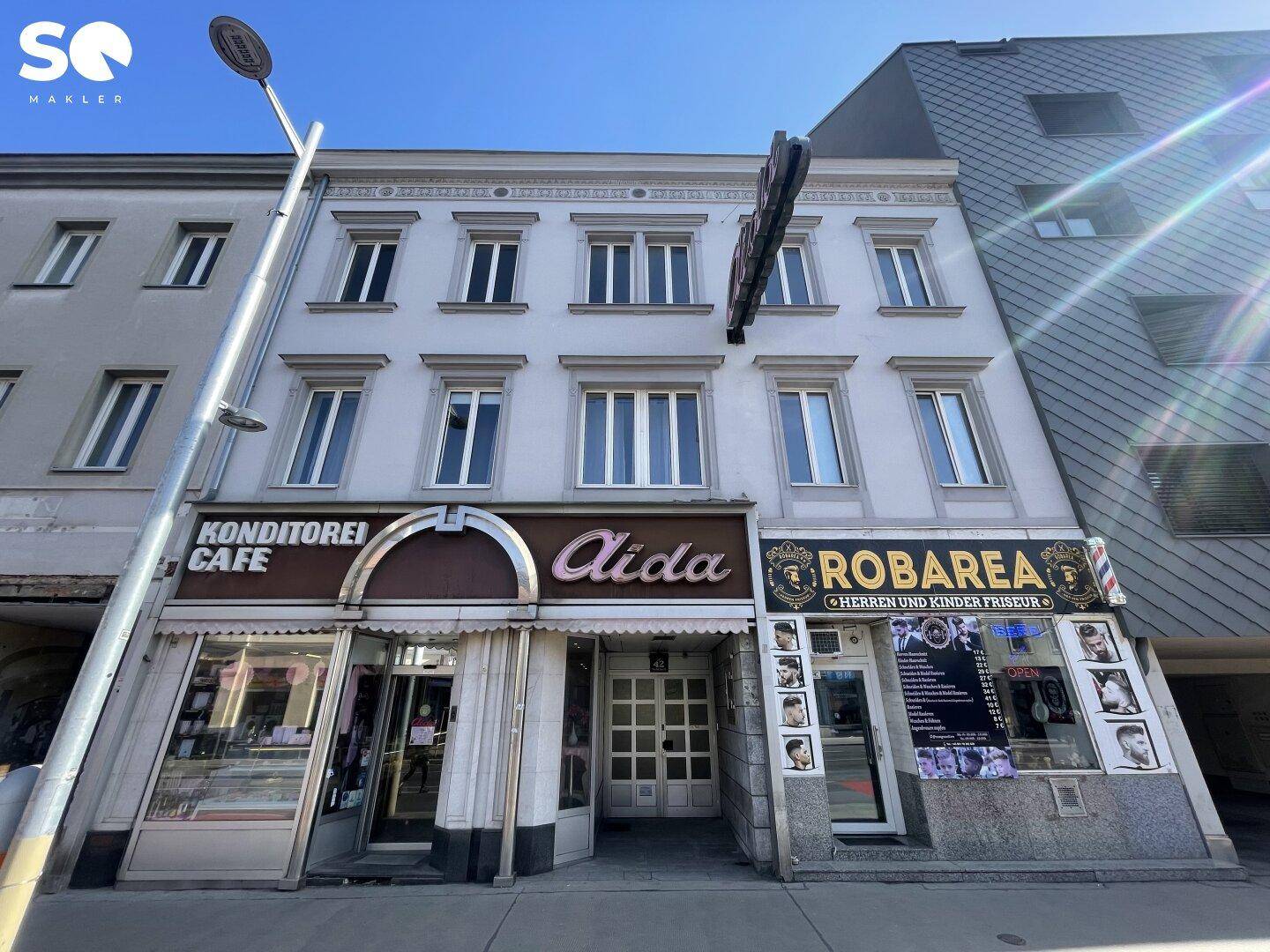Fassade eines Altbaus mit mehreren Gewerbeflächen im Erdgeschoss unter strahlendem Sonnenschein.