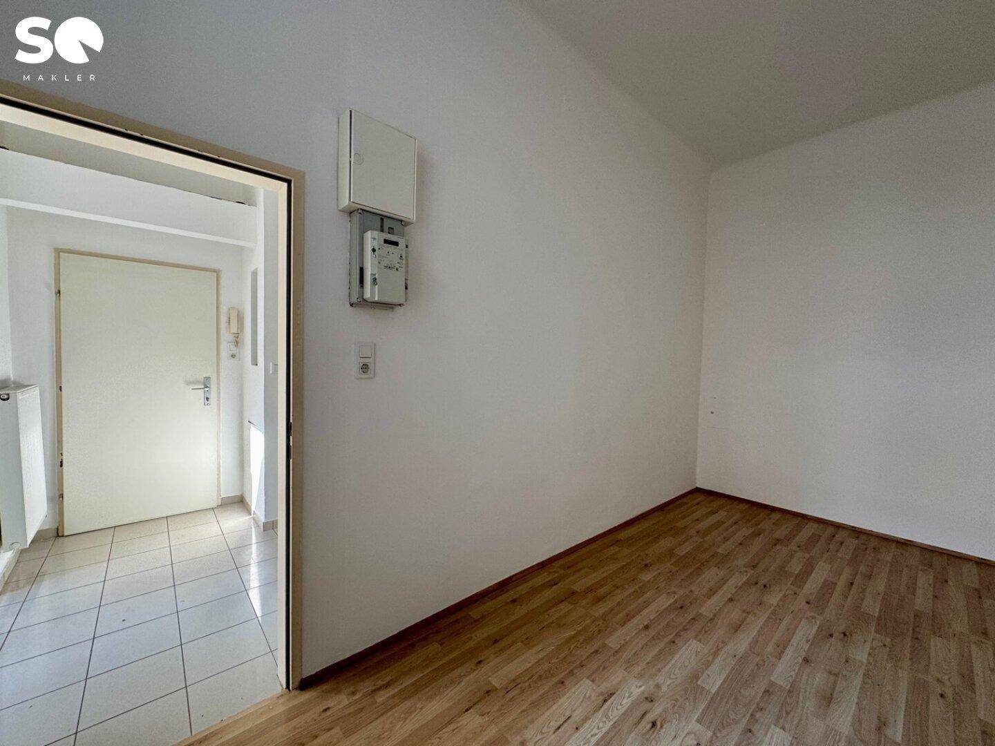 Eingangsbereich mit Fliesenboden und Blick in ein angrenzendes Zimmer mit Holzfußboden.