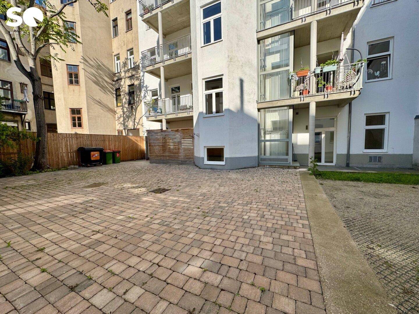 Außenansicht des Gebäudes mit gepflastertem Hof und Balkonen an der Fassade.