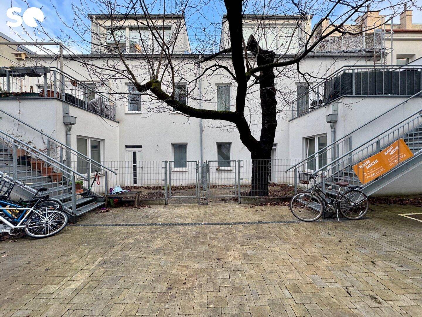 Winterlicher Innenhof mit kahlem Baum und Außentreppen, die zu den Wohnungen führen.