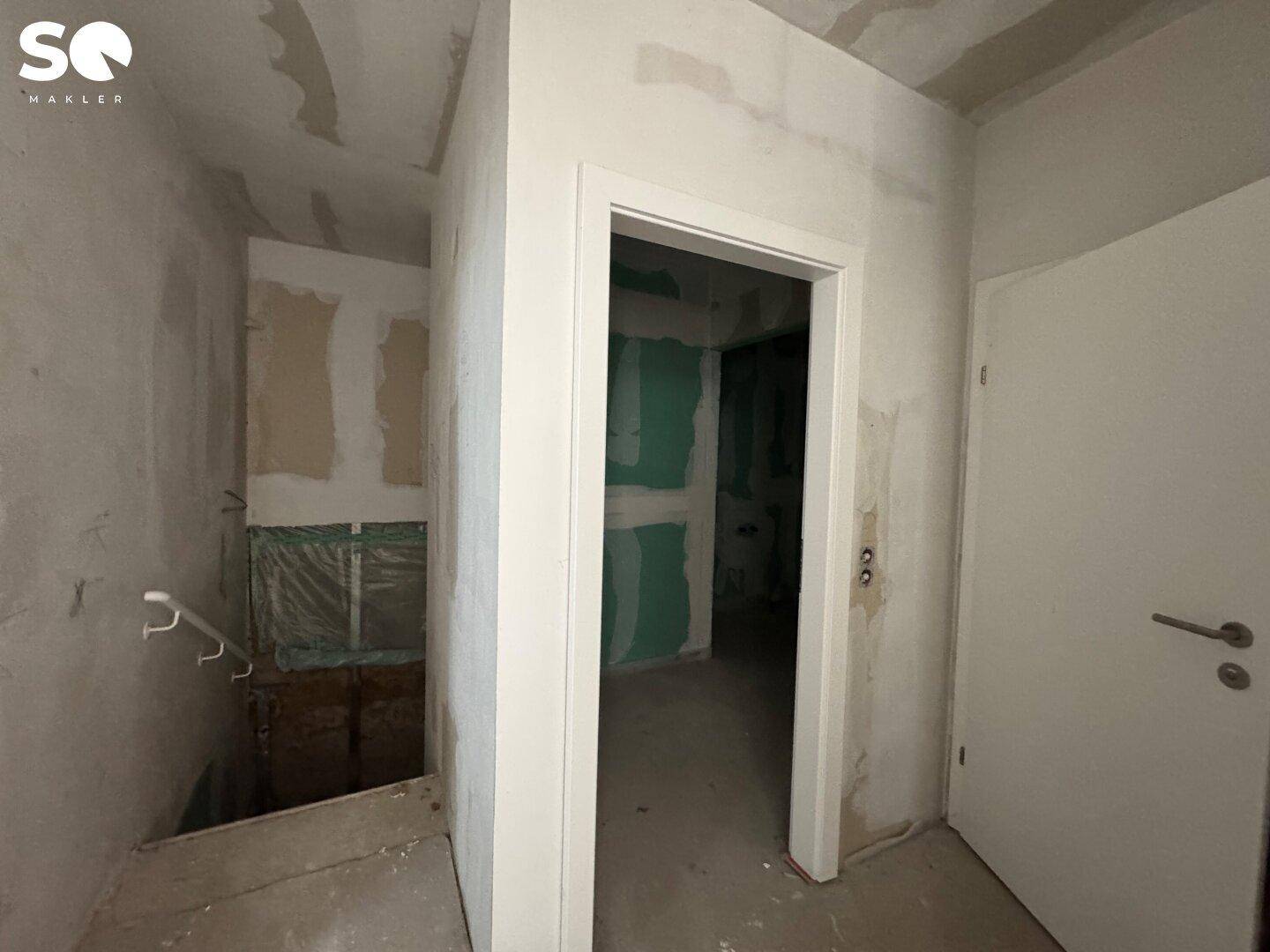 Flurbereich im Rohbau mit offenem Türrahmen und Treppenansatz, bereit für den Ausbau.