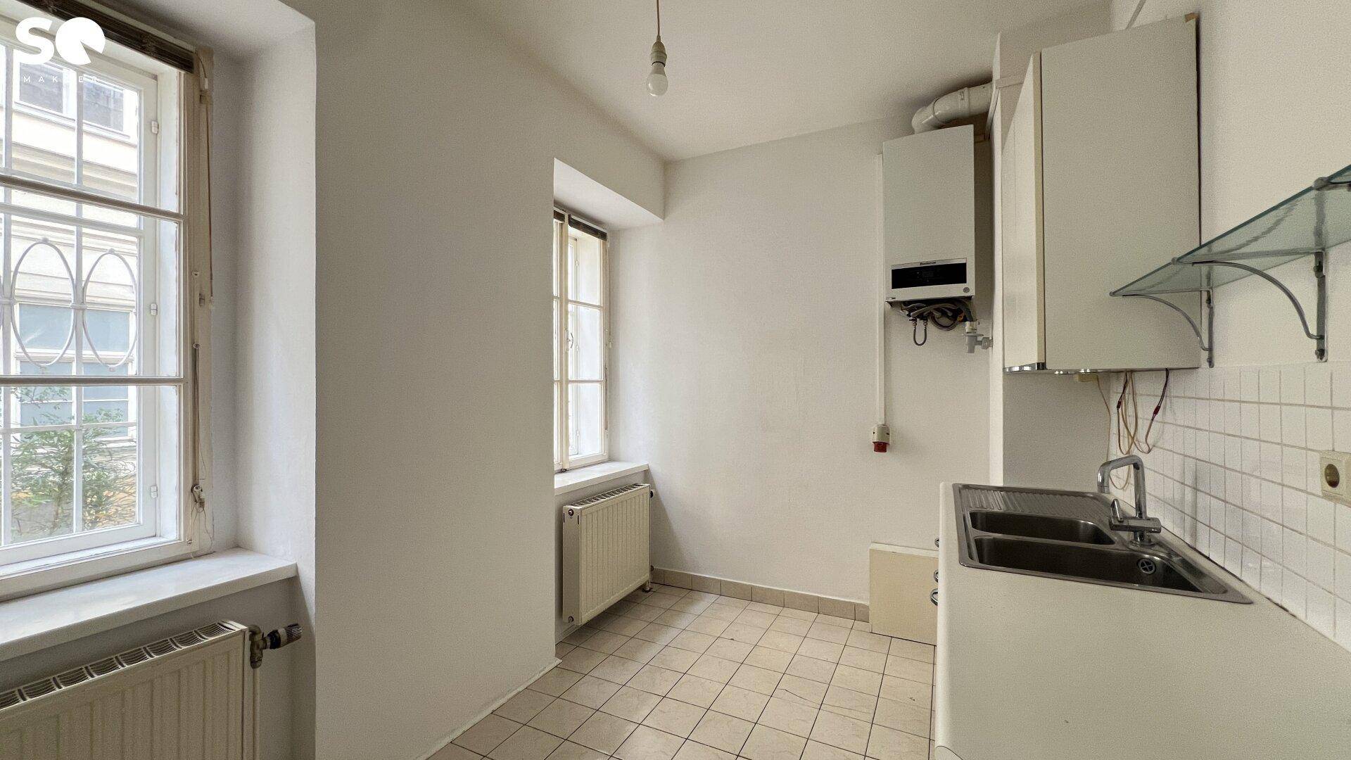 Einfache Küche mit Fliesenboden, Spülbecken und Gastherme, bereit zur Modernisierung.