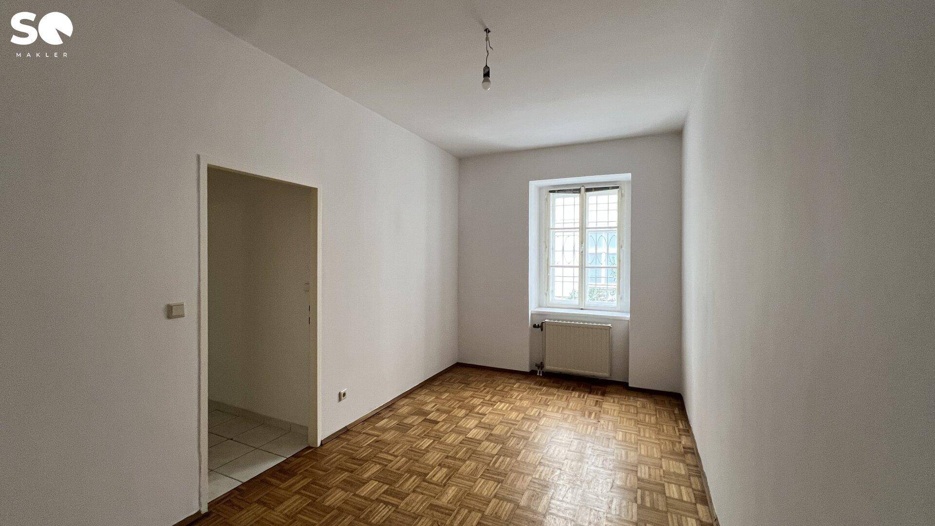 Helles Schlafzimmer mit Parkettboden und Zugang zu einem weiteren Bereich.