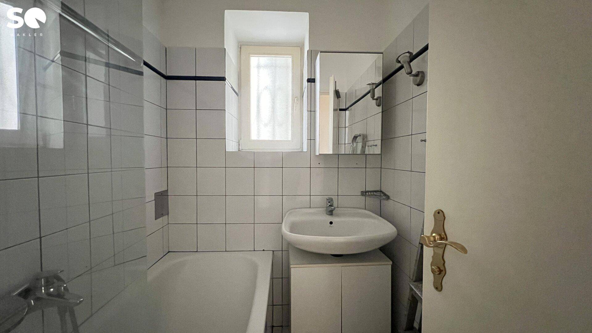 Badezimmer mit Badewanne, Waschbecken und Fenster, komplett gefliest in Weiß.